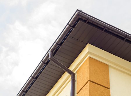 Close-up detail of cottage house corner with brown metal planks siding and roof with steel gutter rain system. Roofing, construction, drainage pipes installation and connection concept.